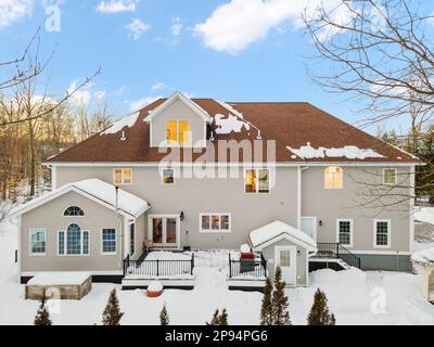 Ein zweistöckiges weißes Haus, umgeben von schneebedeckten Bäumen und Sträuchern in New England Stockfoto