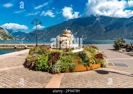 Brunnen mit Blumen, Promenade und Zentrum in Limone sul Garda, hinter Monte Baldo, 2218 m, Gardasee, Provinz Brescia, Lombardei, Italien, Europa Stockfoto