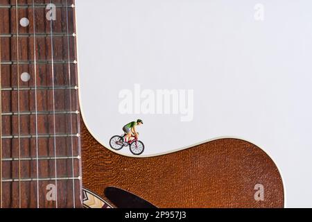 Ein Mann fährt ein Rennrad auf einer Akustikgitarre mit weißem Hintergrund Stockfoto