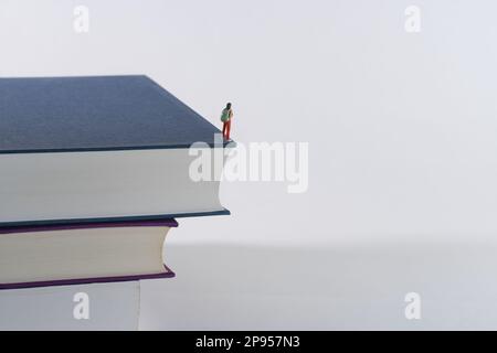 Mann mit Rucksack, Tourist, Anhalter schaut aus einem großen Stapel Bücher, weißer Hintergrund Stockfoto