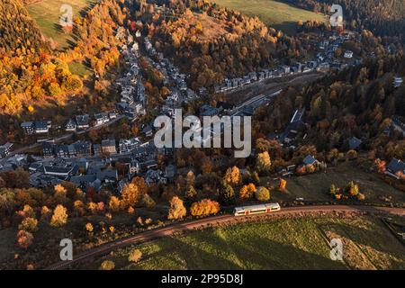 Deutschland, Thüringen, Lauscha, Kleinstadt, Zug fährt im letzten Sonnenlicht über der Stadt, schräge Aussicht Stockfoto