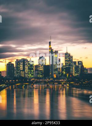 Blick über den Main zu den Wolkenkratzern der Stadt Frankfurt am Main bei Sonnenuntergang, Skyline beleuchtet im Hintergrund Stockfoto