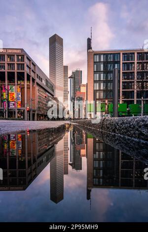 Reflexionen in Frankfurt am Main. Die Stadt, Straßen und Wolkenkratzer spiegeln sich nach Regen in den Pfützen der Straßen wider. Bankenviertel und Wolkenkratzer am Morgen Stockfoto