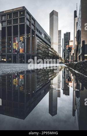 Reflexionen in Frankfurt am Main. Die Stadt, Straßen und Wolkenkratzer spiegeln sich nach Regen in den Pfützen der Straßen wider. Bankenviertel und Wolkenkratzer am Morgen Stockfoto