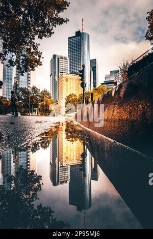 Reflexionen in Frankfurt am Main. Die Stadt, Straßen und Wolkenkratzer spiegeln sich nach Regen in den Pfützen der Straßen wider. Bankenviertel und Wolkenkratzer am Morgen Stockfoto