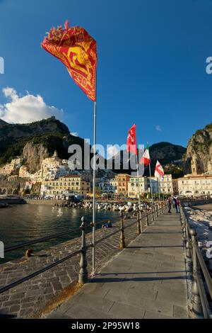 Venezianische Flagge auf einem Fahnenmast auf dem Hauptsteg in Amalfi, Salerno, Italien, mit der Stadt dahinter. Amalfiküste. Tyrrhenisches Meer. Stockfoto