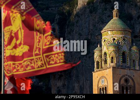 Glockenturm des Duomo di Sant Andrea (St. Andrew's Cathedral). Amalfi, Salerno, Italien Amalfiküste. Die Kathedrale, die im 9. Und 10. Jahrhundert begann, wurde mehrmals ergänzt und umgestaltet und überlagert arabisch-normannische, gotische, Renaissance- und Barockelemente, Und schließlich eine neue normannisch-arabisch-byzantinische Fassade aus dem 19. Jahrhundert. Die venezianische Flagge bläst im Wind Stockfoto