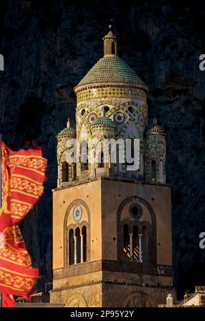 Glockenturm des Duomo di Sant Andrea (St. Andrew's Cathedral). Amalfi, Salerno, Italien Amalfiküste. Die Kathedrale, die im 9. Und 10. Jahrhundert begann, wurde mehrmals ergänzt und umgestaltet und überlagert arabisch-normannische, gotische, Renaissance- und Barockelemente, Und schließlich eine neue normannisch-arabisch-byzantinische Fassade aus dem 19. Jahrhundert. Die venitianische Flagge weht im Wind Stockfoto