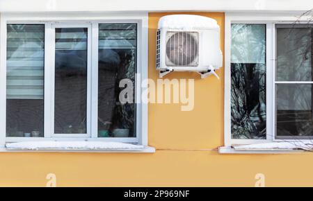 An der Wand des Wohngebäudes ist eine Klimaanlage installiert. Winter und schneebedeckte Fenster des Hauses Stockfoto