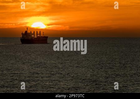 Sonnenuntergang über dem Wasserhimmel mit einem Massengutfrachter, der wegfährt Stockfoto