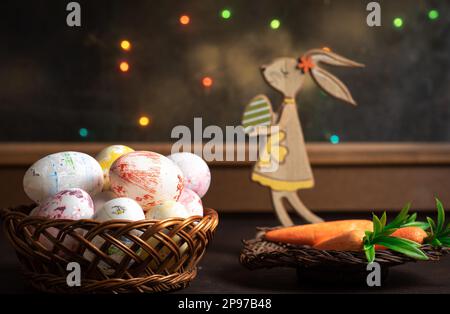 Osterdekoration. Ein hölzerner Hase mit bunten Ostereiern vor dem Fenster auf einem Holztisch. Stockfoto