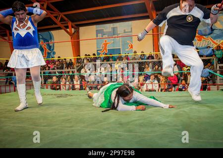 Lucha Libre. Der Schiedsrichter tritt die Hand der Algela la Folclorista hinunter, während eines Kampfes zwischen dem Transvestiten und der Cholita Angela la Folclorista Stockfoto