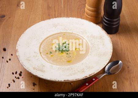 Pilzcremesuppe auf Holztisch. Pilzcremesuppe mit Grün auf weißem Teller auf Holzhintergrund. Cremige Suppe aus Champignons, Gemüse Stockfoto