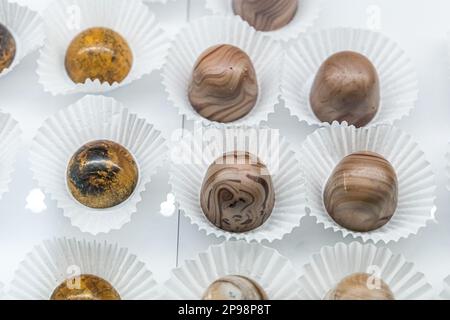 Ein Schokoladenkonfekt und Backglas mit handgefertigten individuellen Trüffeln in verschiedenen Farben und Geschmacksrichtungen mit weißen Papierverpackungen Stockfoto