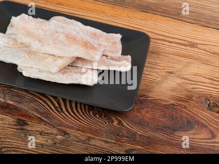 Gefrorener Fisch auf Holzbrett, Weißdorschfilet, gefrorenes Seehechtfilet, gefrorenes Pollackfleisch auf rustikalem Holzhintergrund Stockfoto