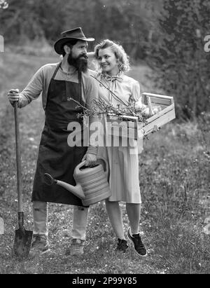 Frau und Mann verbringen Zeit im Obstgarten. Ein Paar Farmen trägt Kisten mit Gemüse und Gemüse entlang des Feldes. Stockfoto