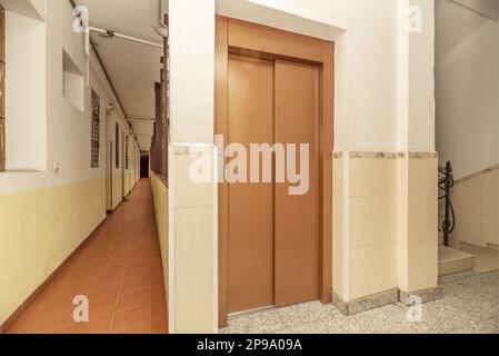 Innenkorridor eines Gebäudes mit Zugangstüren zu Apartments, Steintreppen und Zugangstüren zu einem Aufzug in hellbrauner Farbe Stockfoto