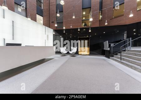 Atrium eines Bürogebäudes mit großem Rezeptionstresen, Granittreppen und Stühlen Stockfoto