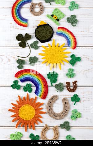 St. Patrick's Day Konzept. Gestrickte Komposition aus grünem Hut, Hufeisen, Sonne, Regenbogen und grünen Shamrocks auf weißem Holzhintergrund. Stockfoto