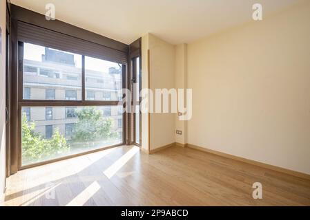 Leeres Wohnzimmer mit einem großen braunen eloxierten Aluminiumfenster mit Fensterläden und Schiebetüren, Eichenboden und cremefarbenen Wänden Stockfoto