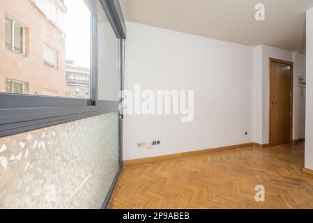 Leeres Wohnzimmer mit einem großen grauen Fenster aus eloxiertem Aluminium mit Glas mit einer durchsichtigen Folie, Eichenboden und glatten weißen Wänden Stockfoto