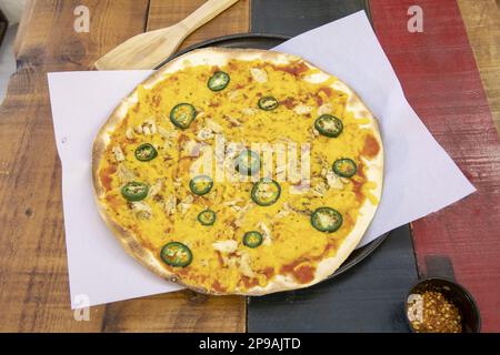 Eine frisch gebackene Pizza mit dünner Kruste und Hühnchen, gelbem Käse, in Scheiben geschnittenen Jalapenos auf einem Backblech aus Pergamentpapier Stockfoto