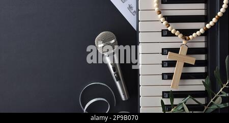 Religiöse Musik mit Klavier und Chöre auf einem schwarzen Tisch, dekoriert mit Olivenzweigen und einem christlichen Kreuz für die Feiertage des Palmensonntags. Draufsicht. Stockfoto