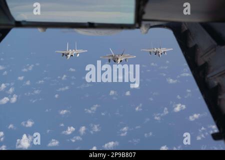 EIN US-AMERIKANISCHER Air Force F-22 Raptor, Mitte, auf der Joint Base Elmendorf-Richardson, Alaska, und zwei F-15C-Flugzeuge auf der Kadena Air Base, Japan, fliegen in Formation über dem indopazifischen Zuständigkeitsbereich, 6. März 2023. Das 6. Air Tanken-Geschwader betankte drei verschiedene Flugzeuge, darunter einen F-15C, F-22 Raptor und einen KC-46A Pegasus. (Foto der US Air Force von Senior Airman Alexander Merchak) Stockfoto