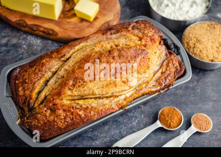 Frisch gebackenes Bananenbrot in der Brotpfanne: Bananenbrot in einer Antihaftpfanne mit Zutaten im Hintergrund Stockfoto