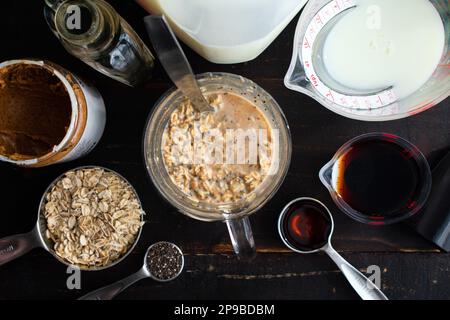 Mischen von Zutaten für Vanilla Cold Brew Overnight Oats in a Glass Tasse: Zubereitung von Haferflocken über Nacht in einem Glasbecher, umgeben von den Zutaten Stockfoto