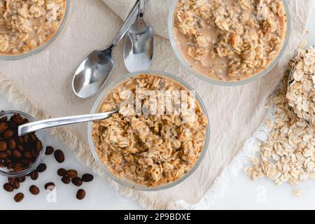 Drei Gerichte Vanilla Cold Brew Overnight Oats: Kleine Glasschüsseln Haferbrei mit Kaffeebohnen, gerolltem Hafer und Löffeln Stockfoto