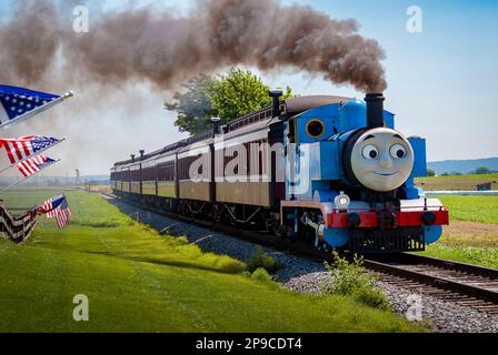 Strasburg, Pennsylvania. Juni 48 2021 - Blick auf Thomas, den Zug, der an einem sonnigen Tag Pkw zieht, während er an amerikanischen Flaggen an einem Zaun vorbeifährt Stockfoto