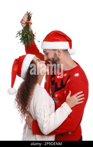 Ein hübsches Paar in Weihnachtsmannhüten unter Mistelzweigen auf weißem Hintergrund Stockfoto