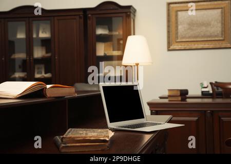 Alte Bücher und Laptop auf Holztisch im Lesezimmer der Bibliothek Stockfoto