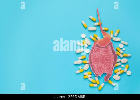 Papierausschnitt von Dünndarm und Pillen auf türkisfarbenem Hintergrund, flach liegend. Platz für Text Stockfoto