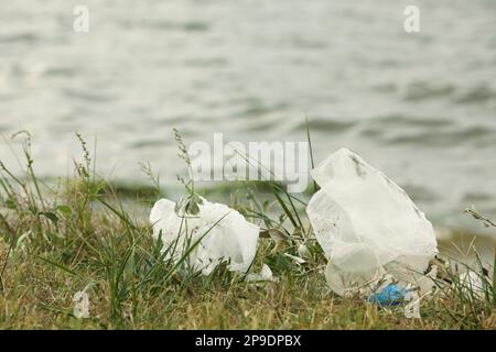 Plastikmüll verstreut auf Gras in der Nähe des Flusses Stockfoto