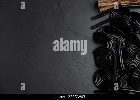 Leckere Süßigkeiten und getrocknete Süßholzwurzeln auf schwarzem Tisch, flach liegend. Platz für Text Stockfoto