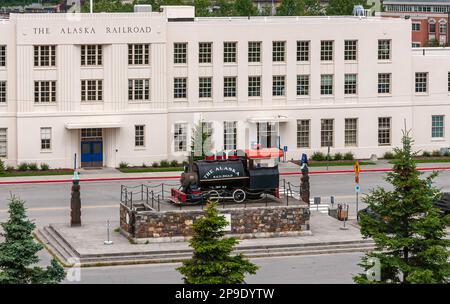 Anchorage, Alaska, USA - 23. Juli 2011: Nahaufnahme, langer weißer Stein Alaska Railroad Depot Gebäude mit alter Lokomotive vor dem Hotel. Grreen fol Stockfoto