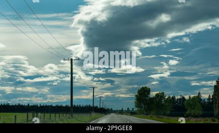 Stürmische Wolken über einer leeren Landstraße, Stromleitungen entlang der Straße. Canterbury. Neuseeland. Stockfoto