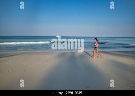 Am frühen Morgen joggt eine einsame asiatische Frau am Kata Noi Beach, Phuket, Südthailand entlang Stockfoto