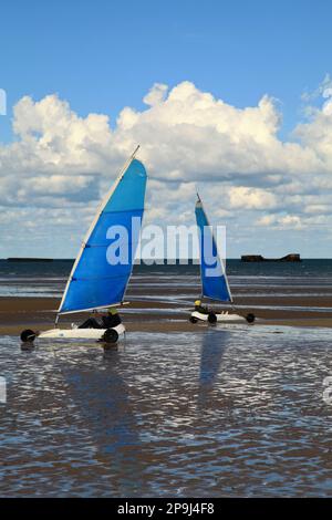 Arromanches, Frankreich - 14 2012. Oktober: Zwei Personen veranstalten ein freundliches Sandyachten-Rennen am Gold Beach in der Normandie. Im Hintergrund können wir immer noch sehen Stockfoto