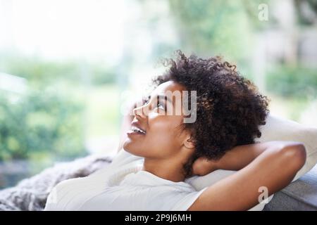 Ich nehme mir etwas Zeit. Eine lächelnde junge Frau, die sich zu Hause entspannt. Stockfoto