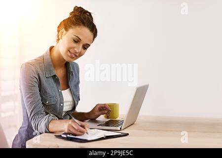 Gehen Sie selbstbewusst in die Richtung Ihrer Träume. Eine junge Frau, die Notizen von ihrem Laptop macht. Stockfoto