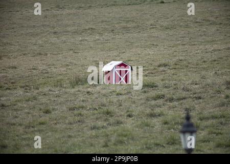 Eine kleine rote Scheune sitzt einsam auf einem Feld. Stockfoto