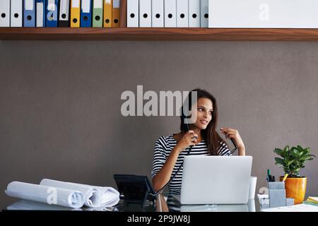 Ihren Klienten einen Fortschrittsbericht zu geben. Eine junge Geschäftsfrau telefoniert, während sie an ihrem Büroschreibtisch sitzt. Stockfoto