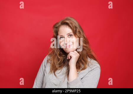 Braune Frau in grauem Pullover auf rotem Studiowandhintergrund Stockfoto