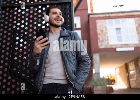 Erfolgreicher europäischer Freiberufler, der im Freien Musik mit Kopfhörern hört Stockfoto