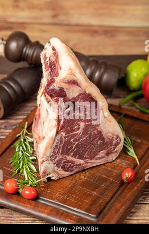 Großes rohes Rindfleisch-T-Bone-Steak. Kalbfleisch-Cowboy-Steak auf dem Rib-Eye-Holz-Präsentationstafel. Weicher T-Bone mit Prime-Cut-Effekt Stockfoto