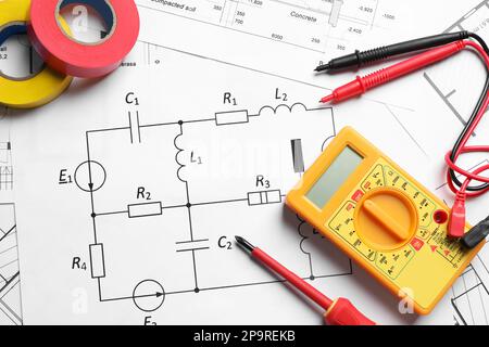 Digitalmultimeter und Klebebänder auf Papierbögen, flach aufgelegt. Elektrikerbedarf Stockfoto