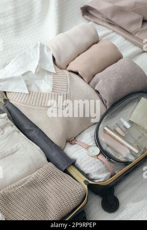 Offener Koffer mit gefalteten Kleidungsstücken und Accessoires auf dem Bett Stockfoto